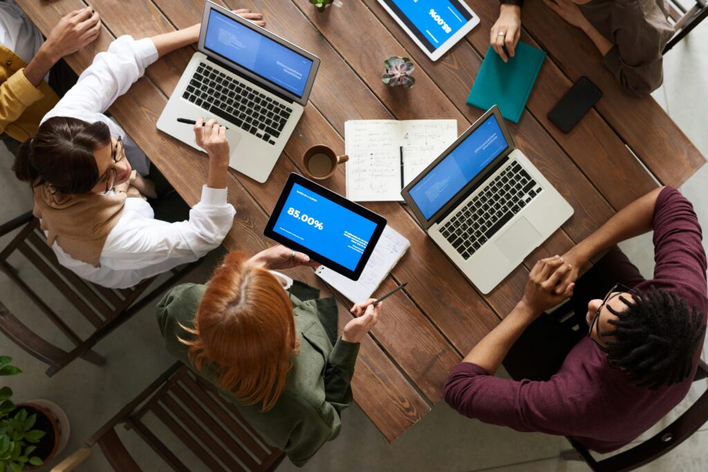 Stock image showing: From the top: People sitting at a table with their laptops engaging and having a meeting.