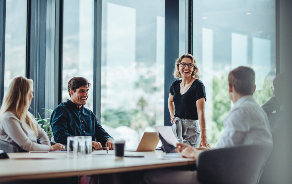 Stock image showing: Office colleagues having casual discussion during meeting in conference room. Group of men and women sitting in conference room and smiling.