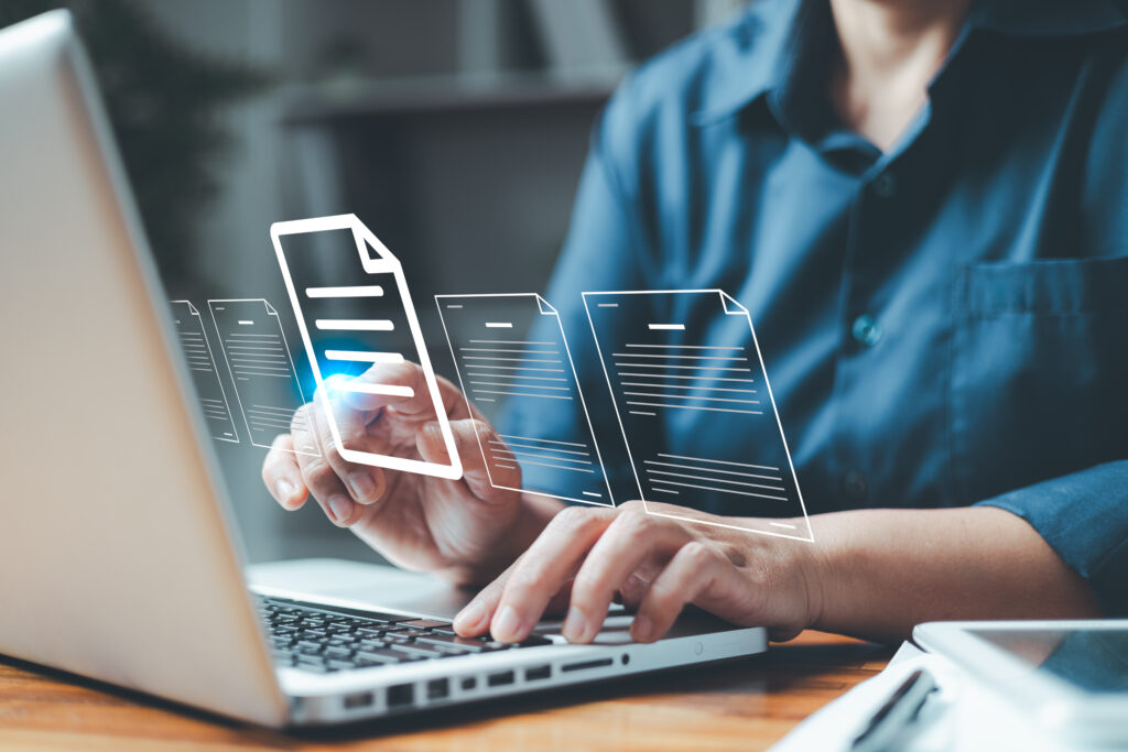 A stock image showing: A person point their finger on one document. This document is bigger and white, the other docments next to it are smaller and grey